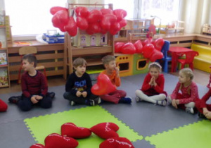 Dzieci siedzące na dywanie po turecku.